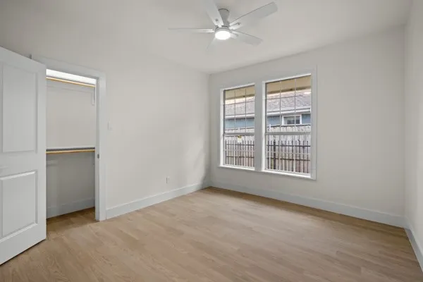 Recessed closet with built-in shelving, wood-finish flooring, dual windows with gridded panes, and a ceiling fan with integrated lighting