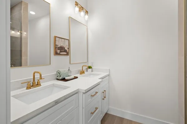 Dual vanity featuring white shaker cabinetry, gold-finish hardware, and integrated rectangular sinks with gold-finish faucets