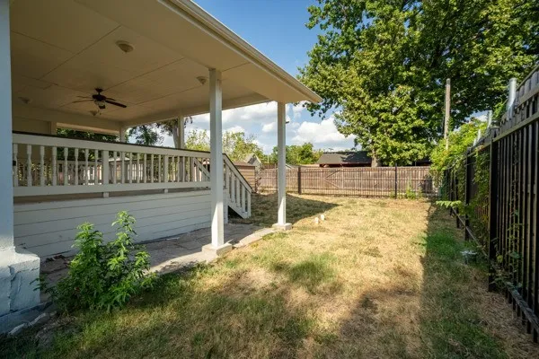 Covered deck with baluster railing and ceiling fan, overlooking a fenced yard with mature trees