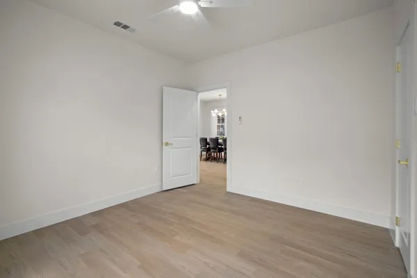 Wood-finish flooring, white walls, white trim, ceiling fan light fixture, and white interior doors with brass hardware