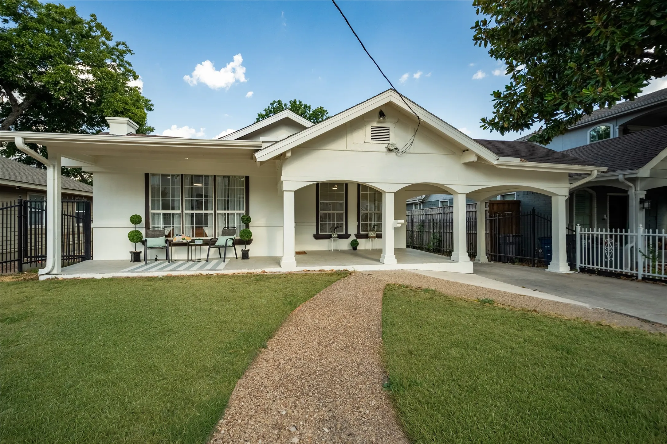 White exterior with dark trim windows, covered porch, arched porte-cochère, gravel walkway, and a manicured lawn