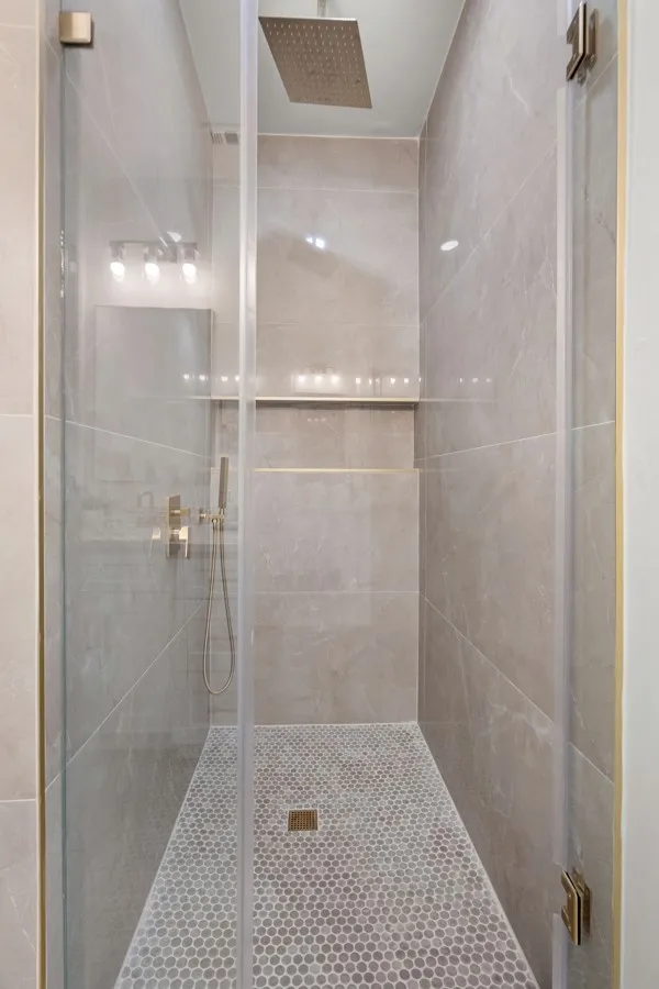 Glass-enclosed shower with a rainfall showerhead, tiled walls, a built-in shower niche, and a hexagonal mosaic tile floor