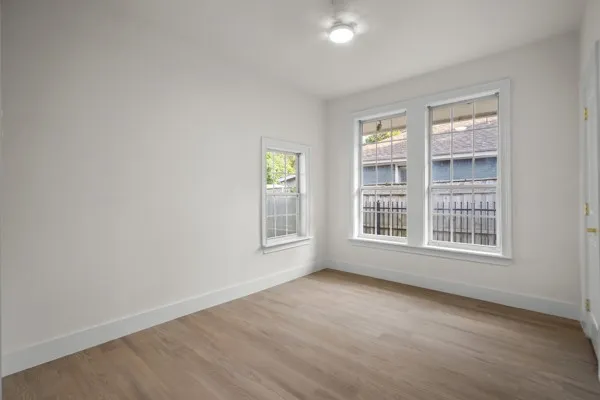Light wood-finish flooring, white walls, multiple windows with white trim, and a flush-mount ceiling light