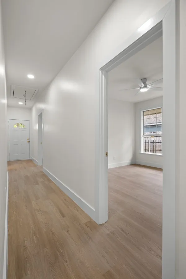 Light wood-finish flooring throughout, recessed ceiling lighting, white interior door, and a ceiling fan in the adjacent room