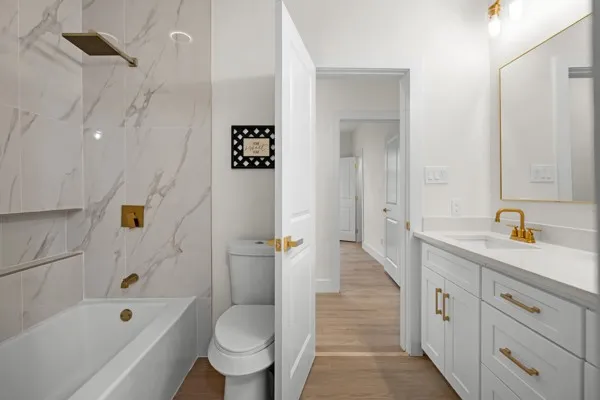 White vanity with gold-finish hardware and faucet, a rectangular mirror, and a white countertop