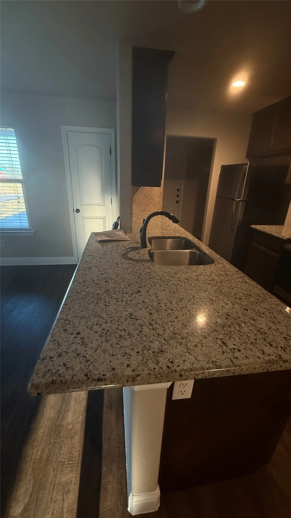 Kitchen island with speckled countertop, stainless steel double basin sink, and black pull-down faucet