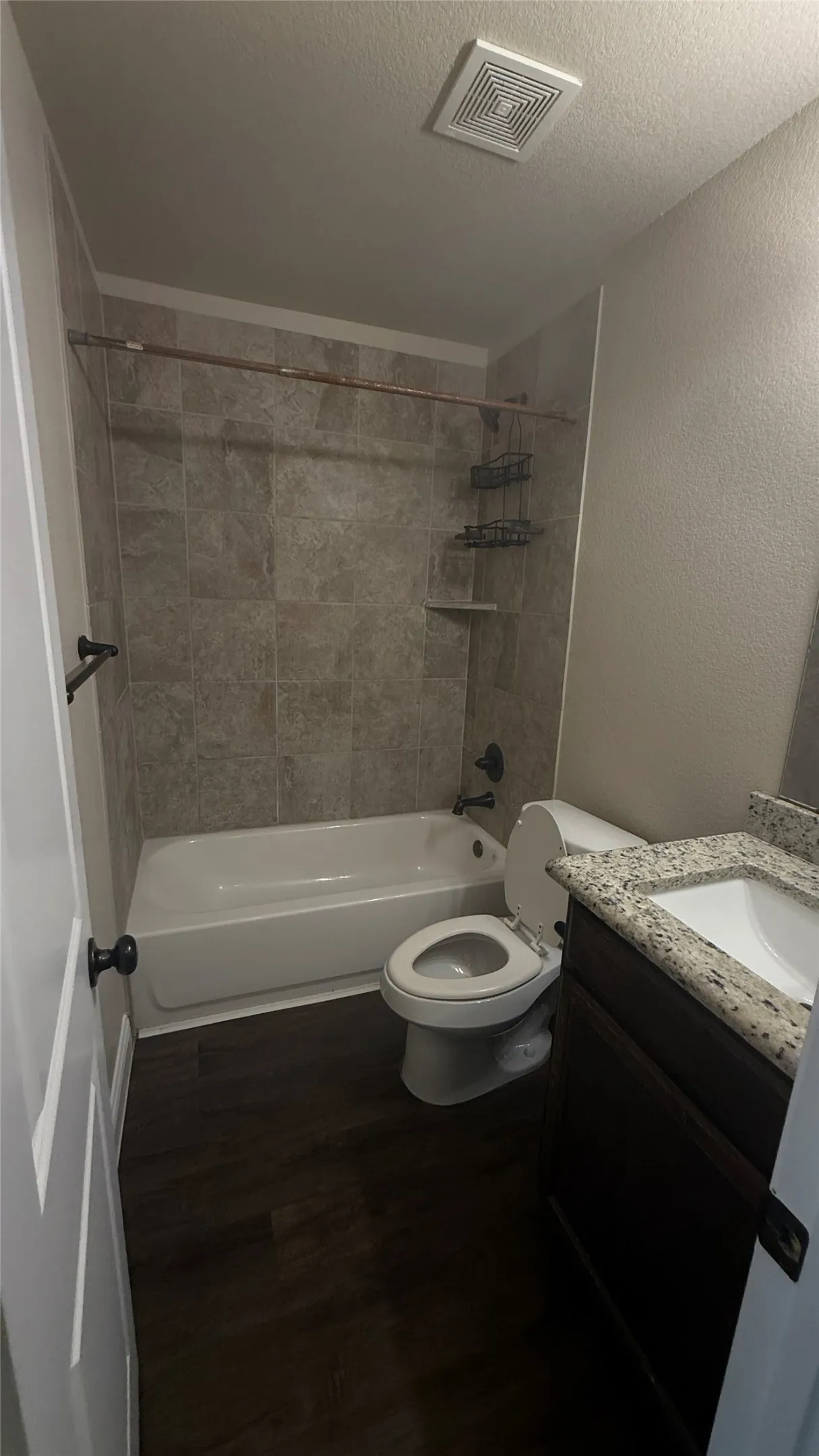 Floor-to-ceiling tiled shower, built-in shower shelving, wood-finish flooring, vanity with integrated sink, and a granite-finish countertop