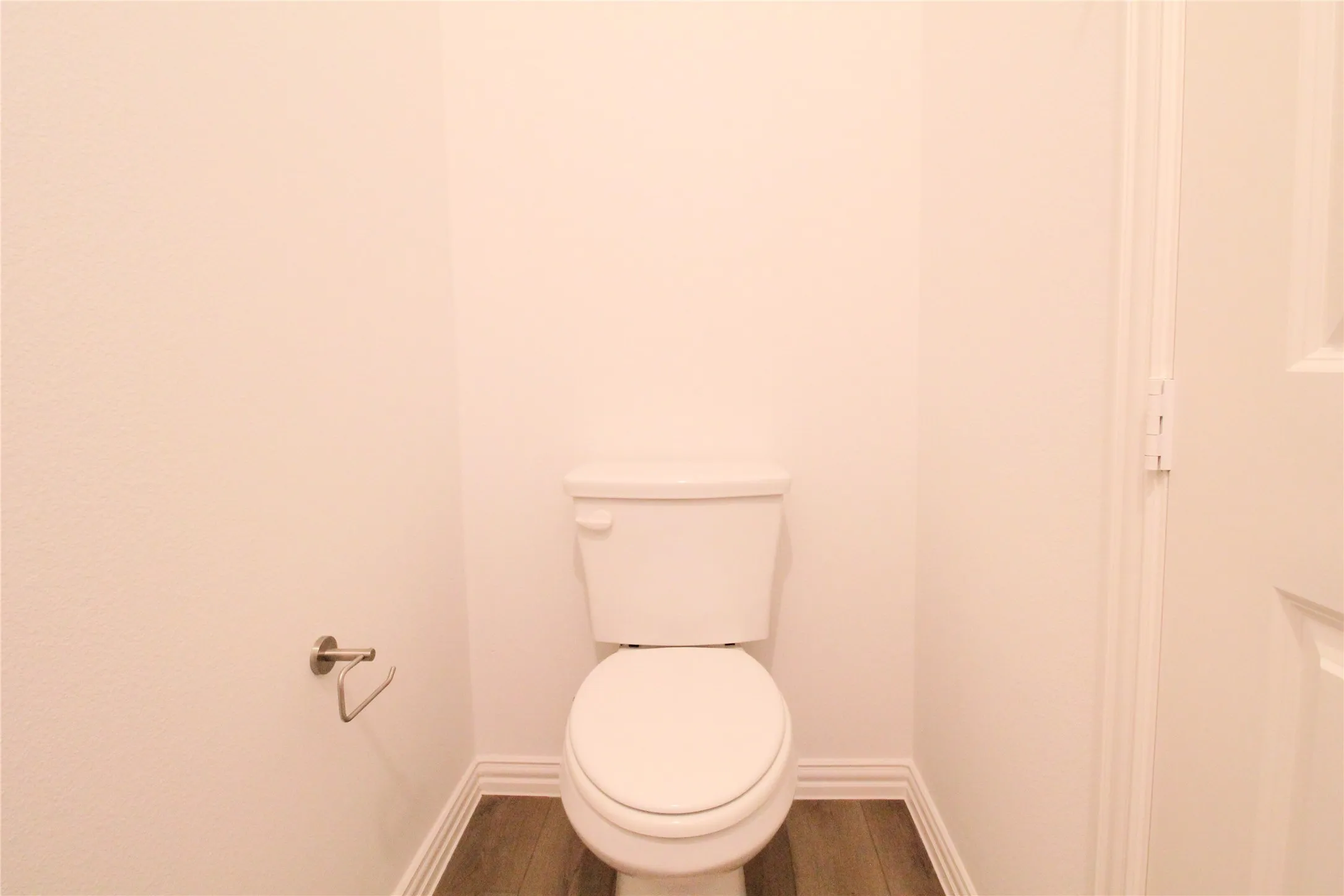 White toilet with wood-finish flooring and white baseboards