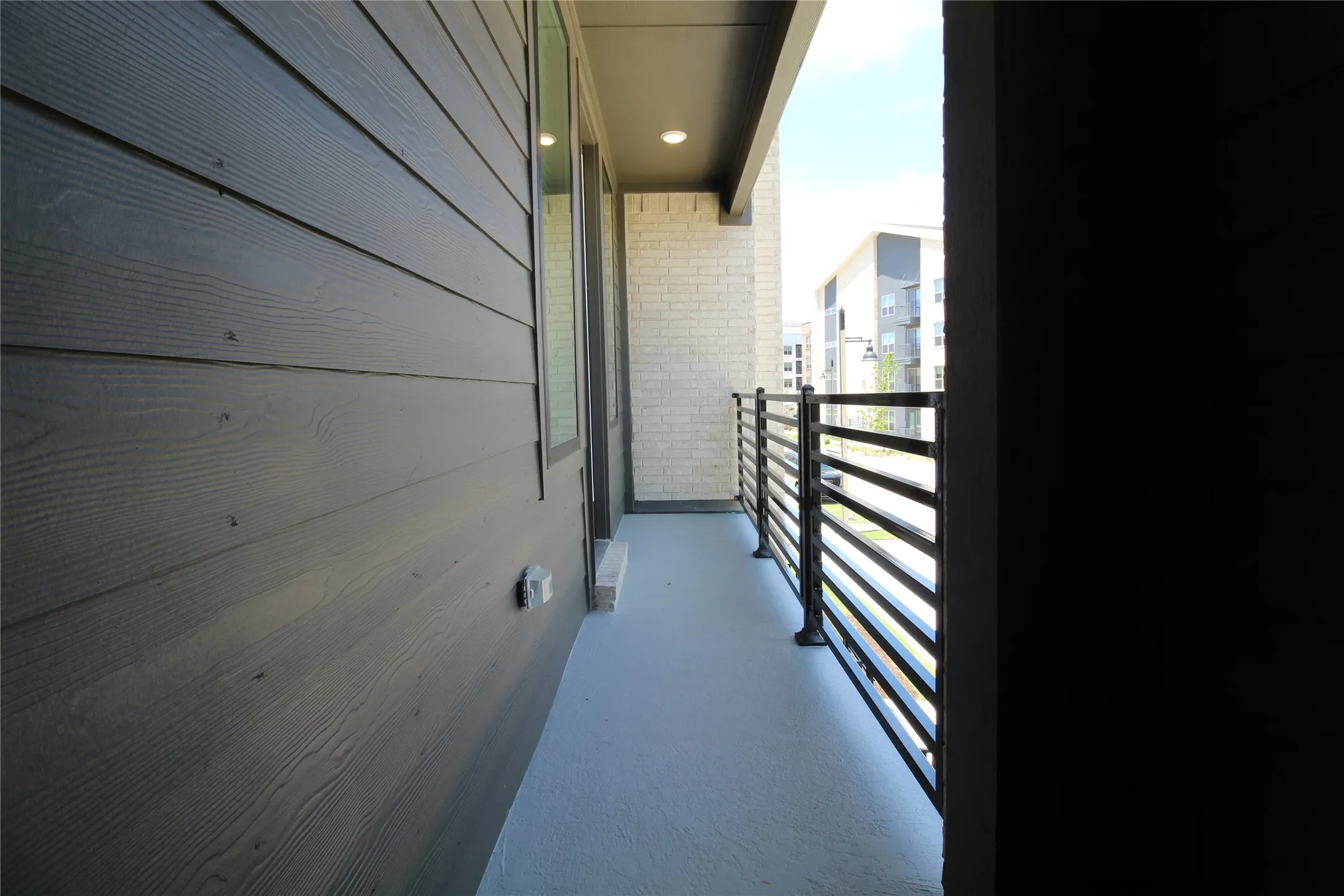 Private exterior balcony with composite decking, featuring sleek horizontal black metal railings and overhead recessed lighting
