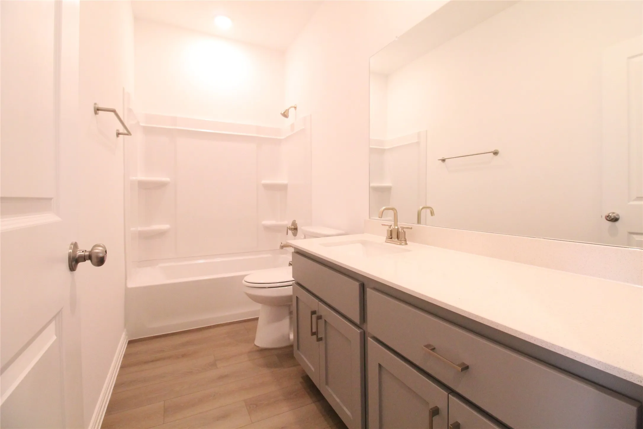 Bathroom featuring a built-in tub with shower, white shower surround, contemporary vanity with a light-toned countertop, brushed nickel faucet, and wood-finish flooring