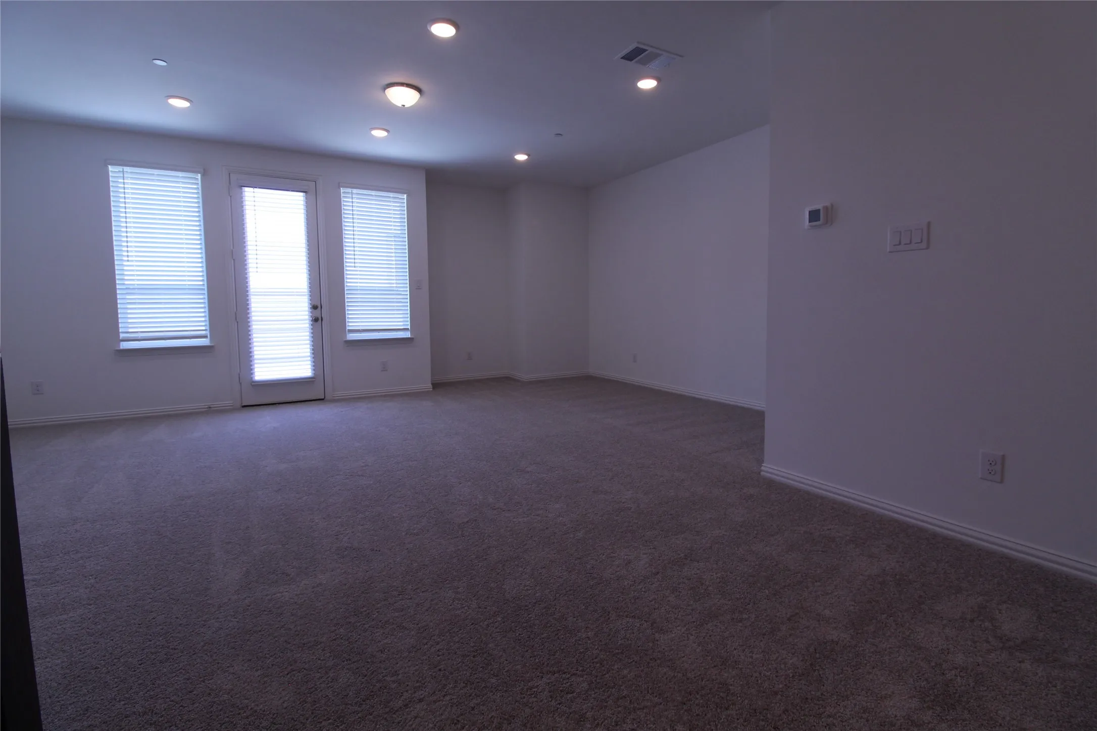 Spacious interior room featuring neutral-toned carpeting, white walls, and recessed lighting