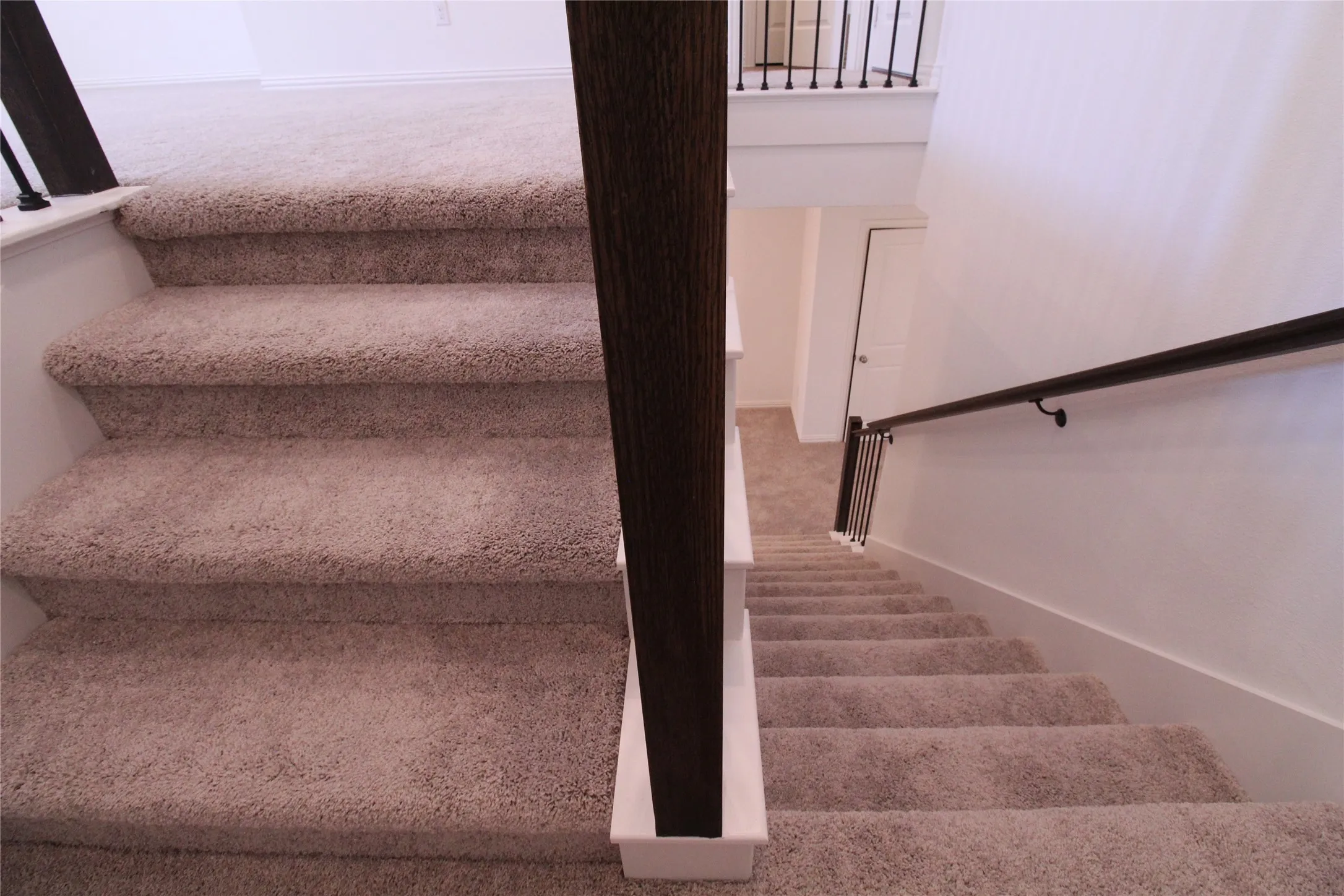 Carpeted staircase with dark wood newel post and black metal balusters