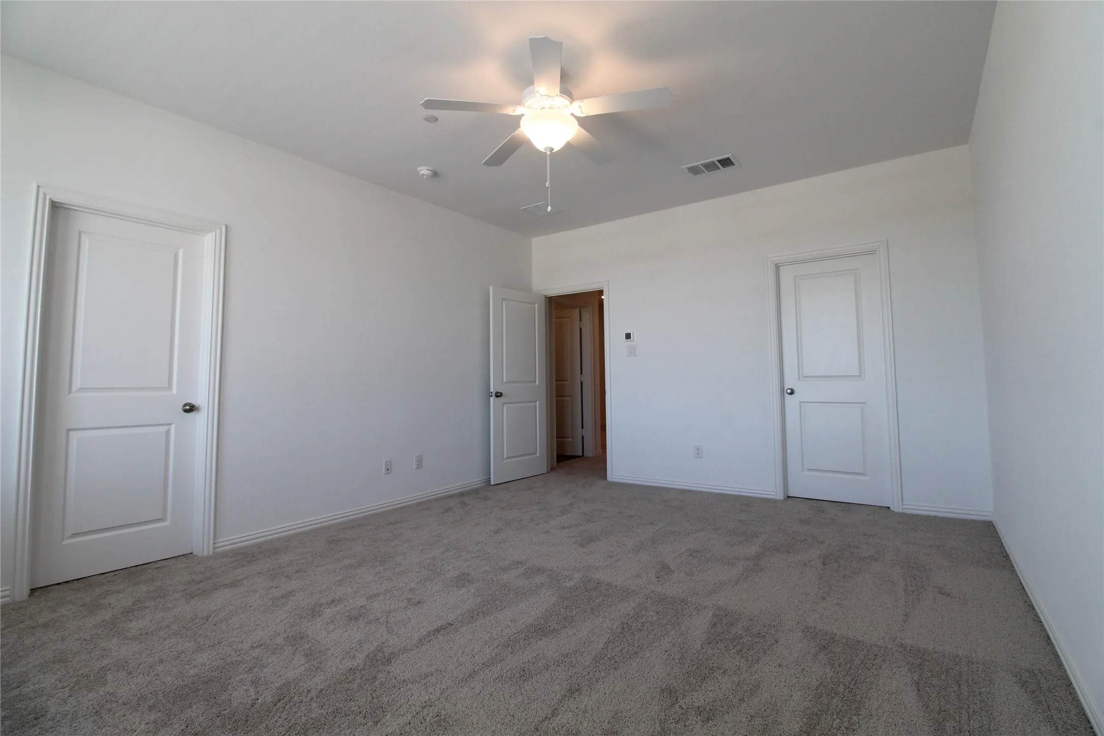 Carpeted interior room featuring a ceiling fan with integrated lighting, white baseboards, and two paneled doors with round hardware