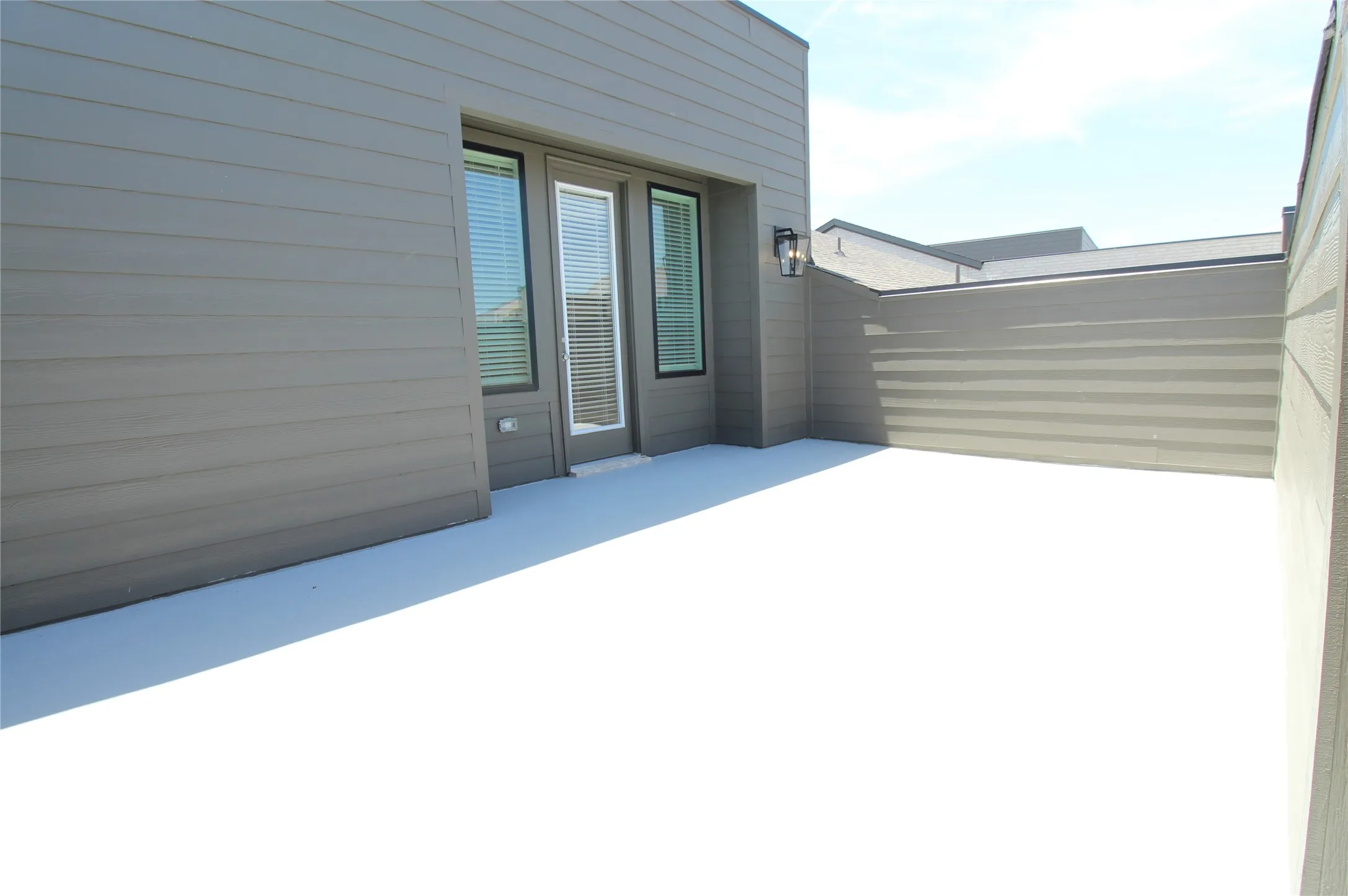 Private exterior patio with grey horizontal siding and a dark framed glass door