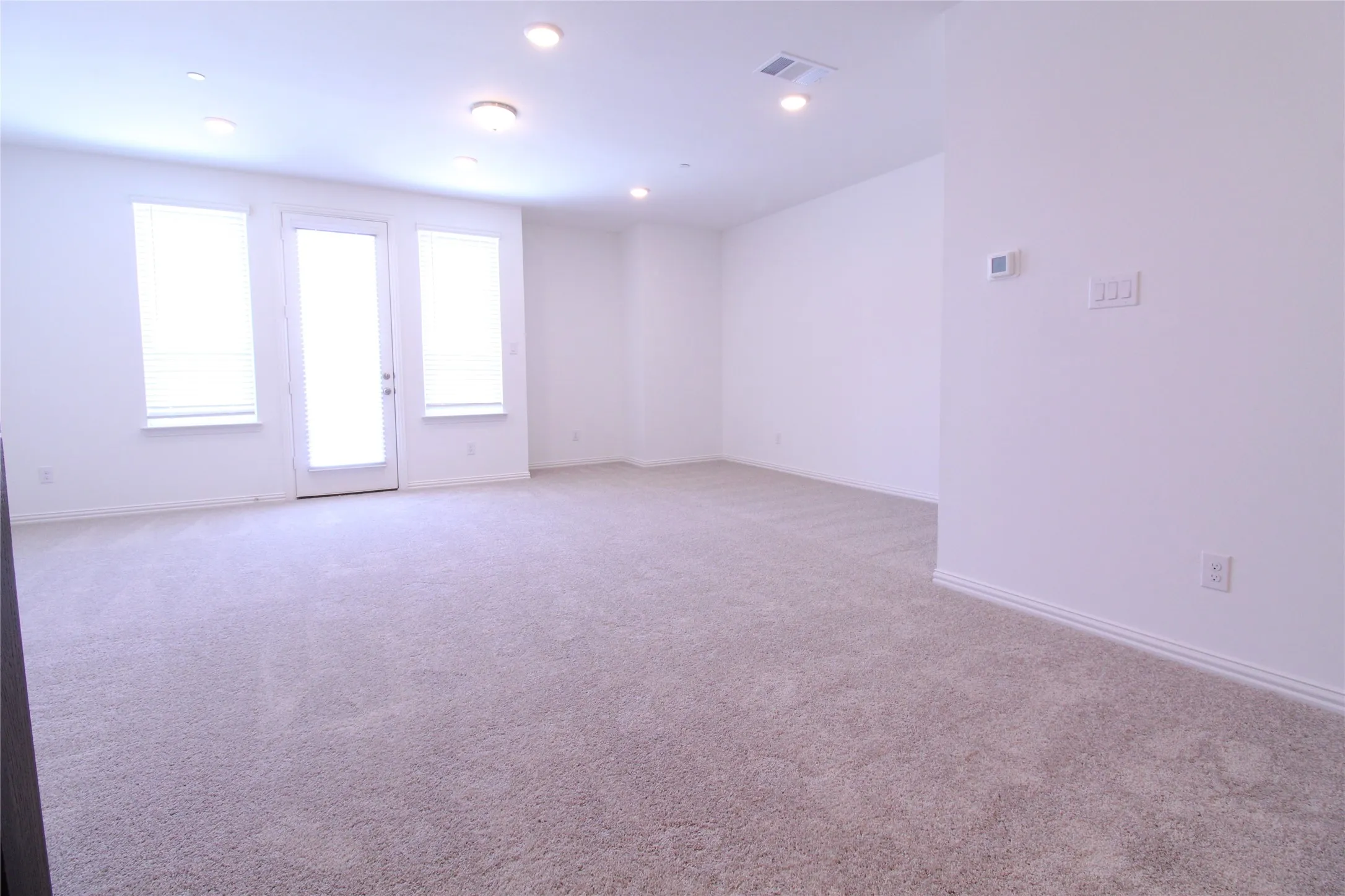 Spacious room featuring neutral carpeting, white walls, recessed ceiling lighting, and a white door with two flanking windows
