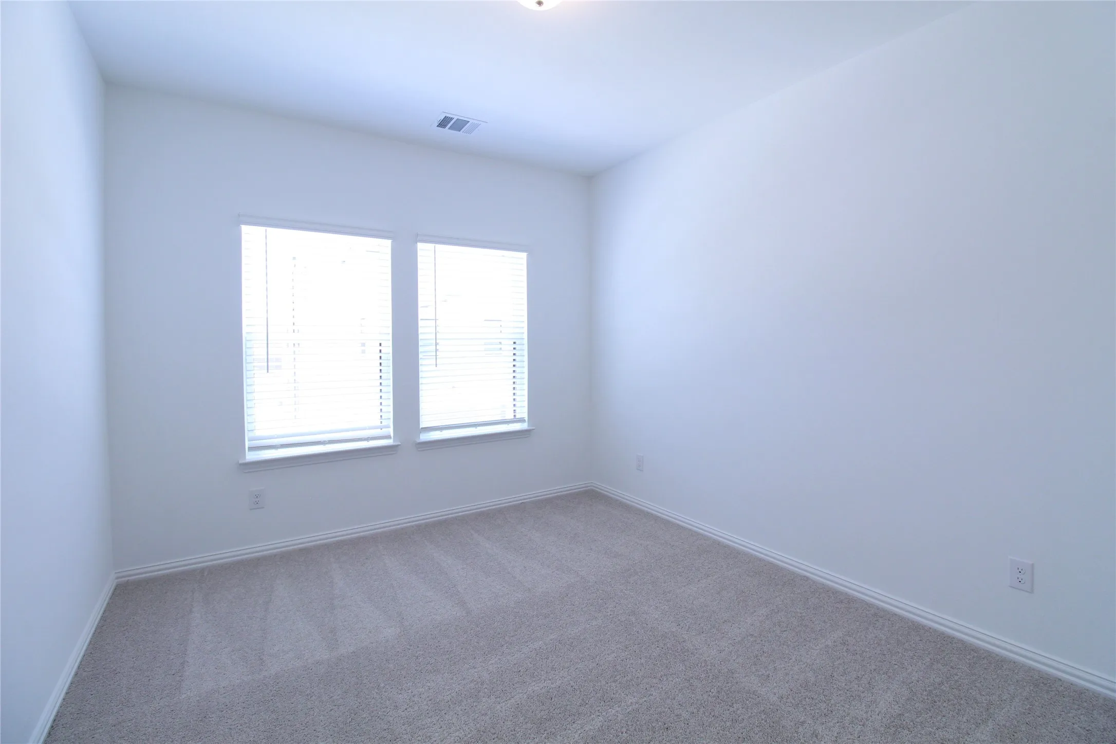Bright room featuring two windows with horizontal blinds, neutral wall paint, light-colored carpet, and white baseboards