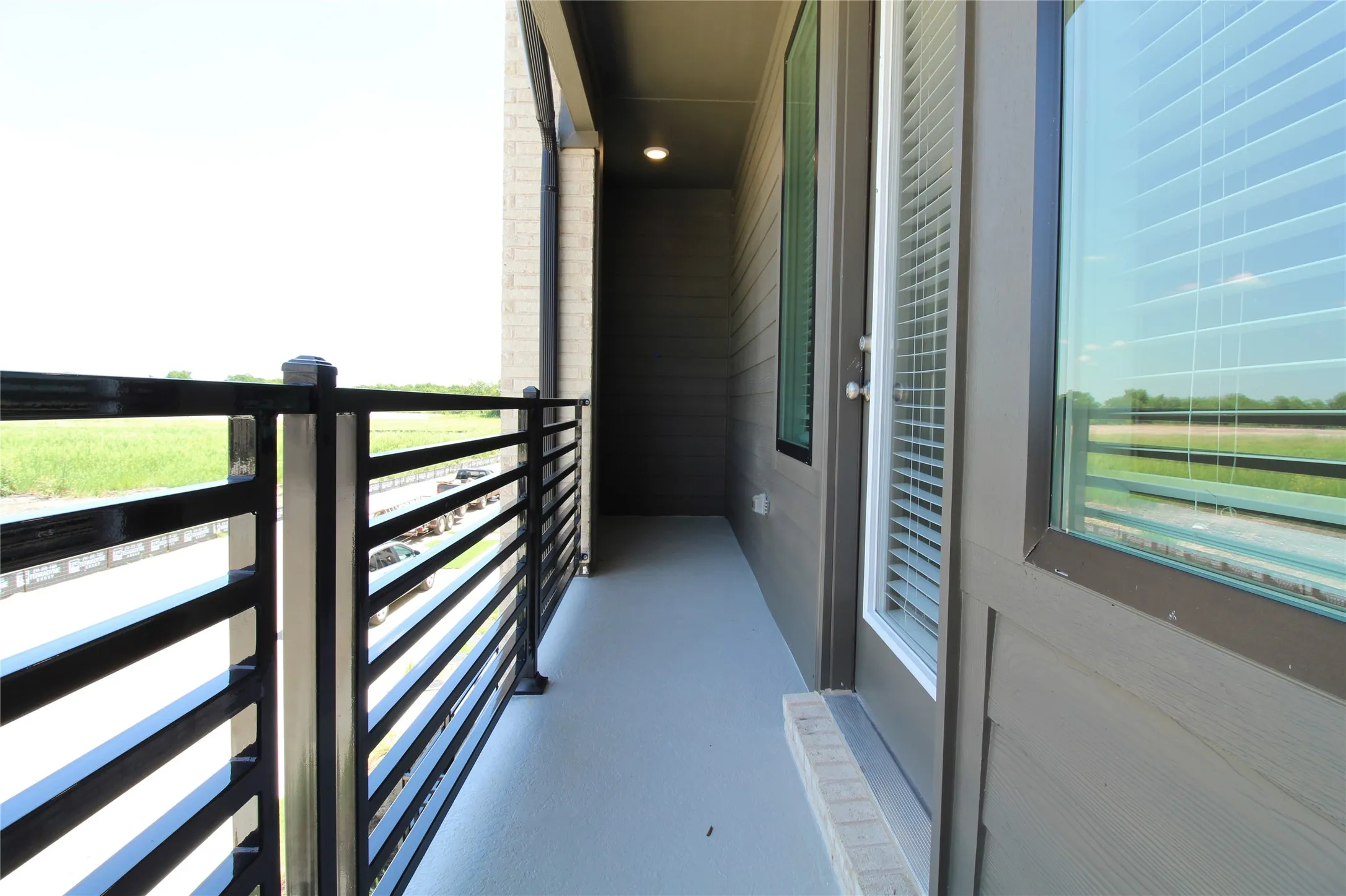 Balcony featuring a black metal horizontal railing, a light gray painted concrete floor, and direct access through a glass-paneled door with integrated blinds