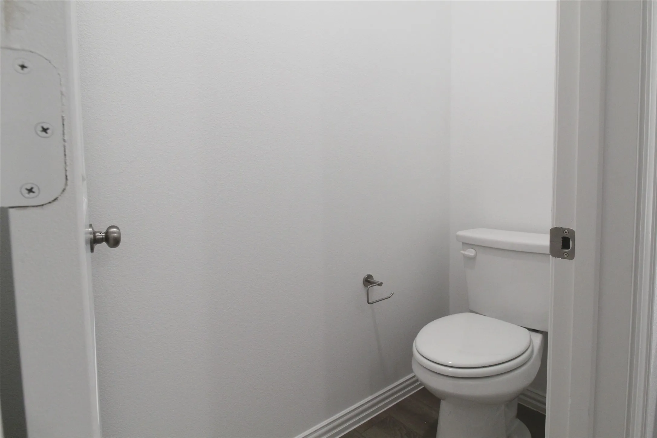 Compact powder room featuring a white toilet, bright white walls, and wood-finish flooring