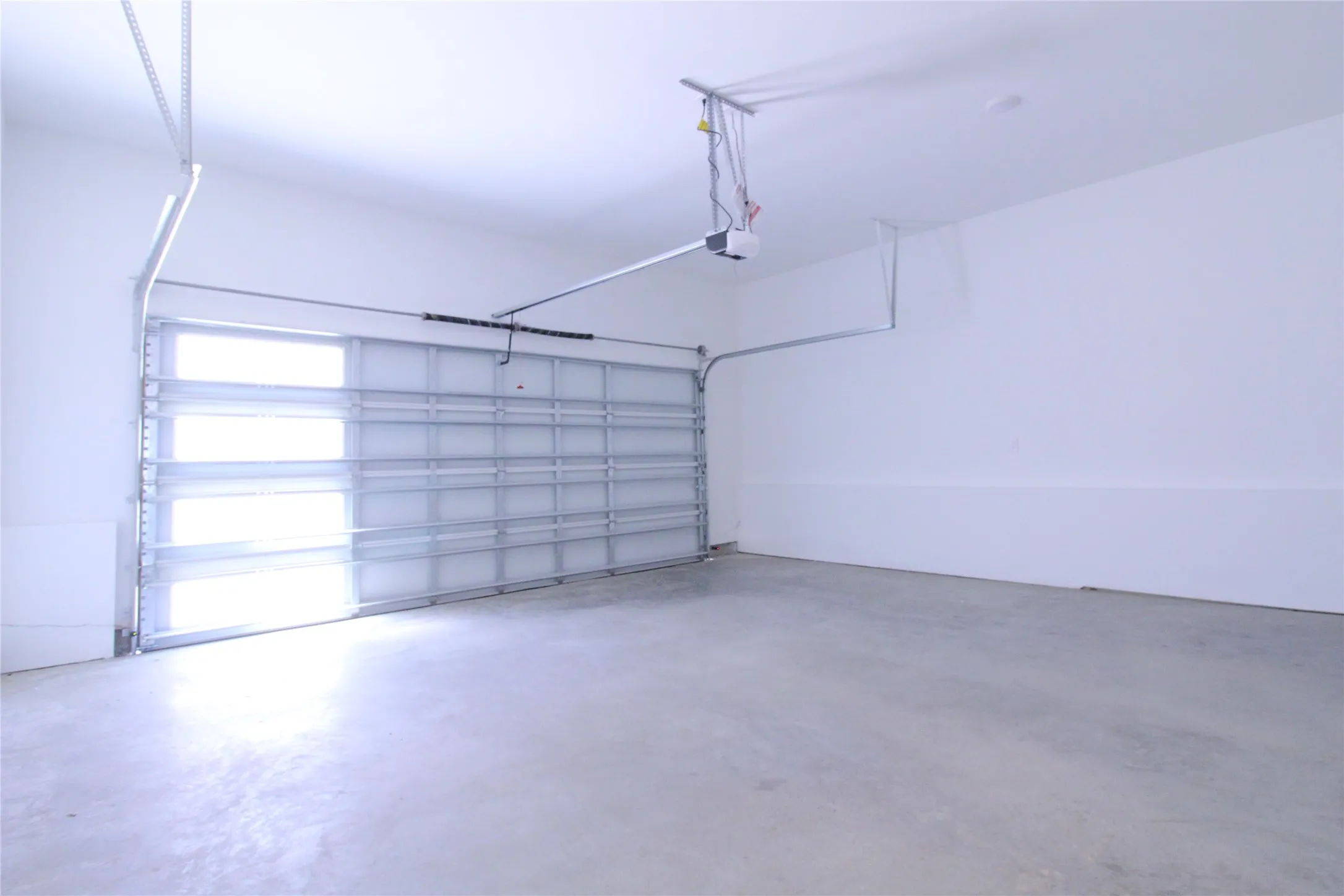 Spacious garage featuring a concrete floor, bright white walls, and an automatic overhead door with integrated frosted glass panels