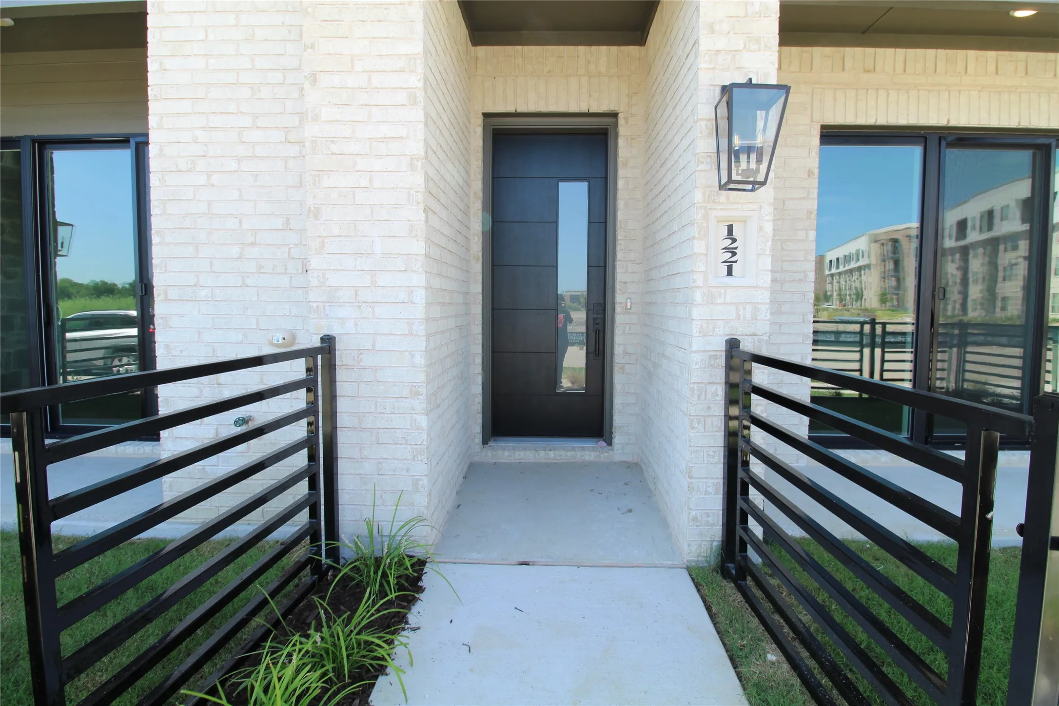 Modern entry featuring a black door with vertical glass insert, white brick facade, and contemporary black metal railing