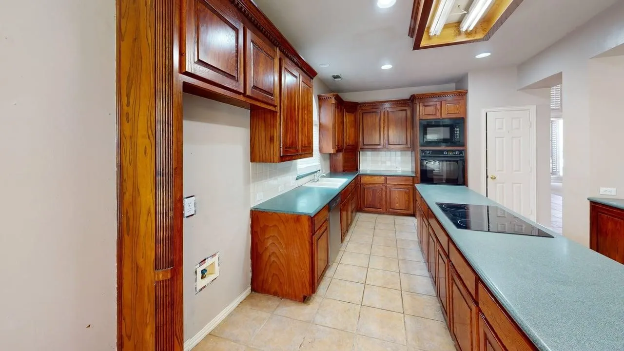 Kitchen featuring extensive cabinetry with paneled doors, tile flooring, built-in appliances, and a cooktop on an extended countertop