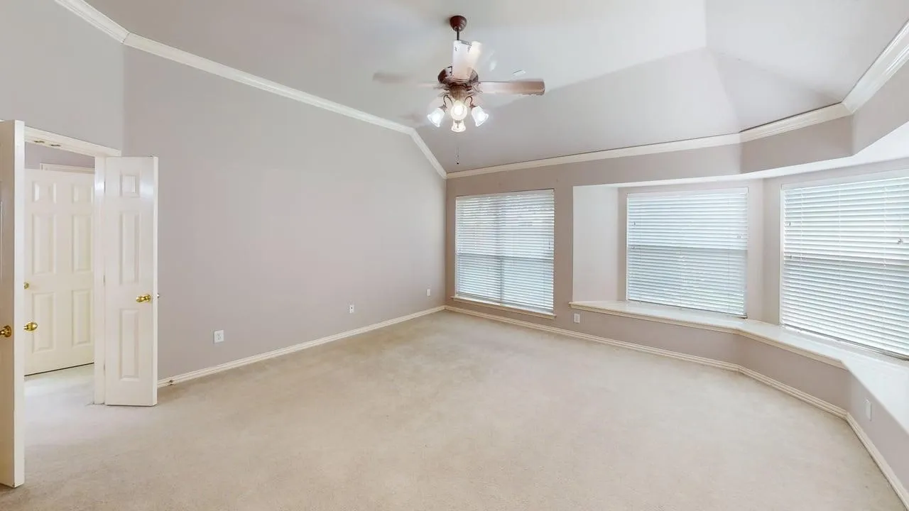 Vaulted ceiling with crown molding, ceiling fan, and carpeted flooring