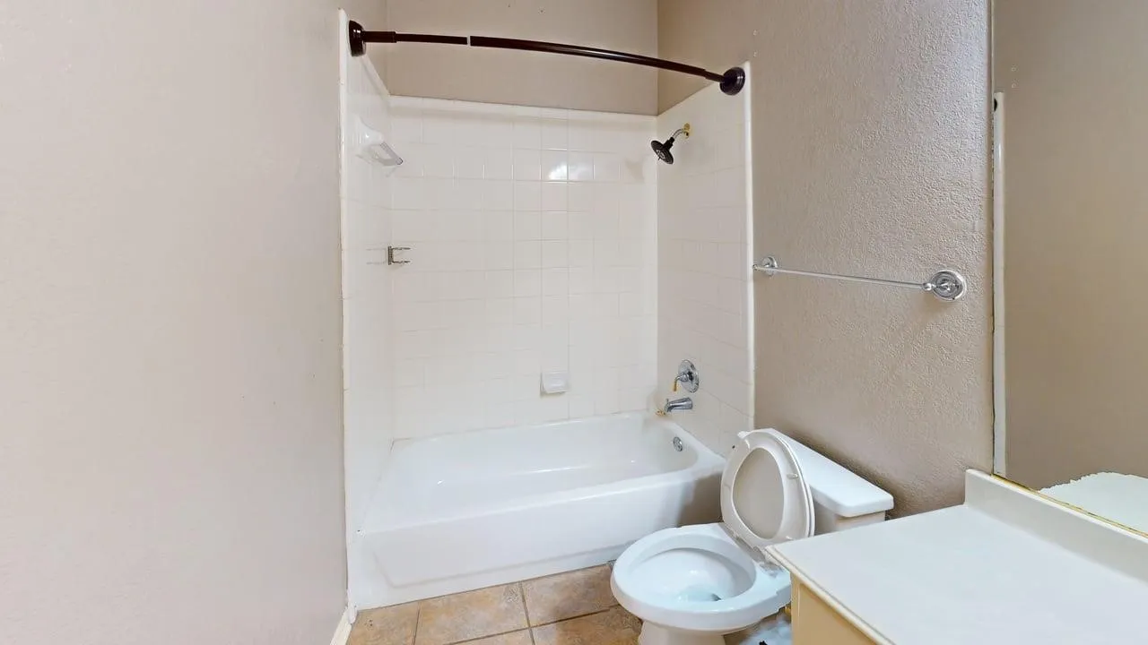 Ceramic tile flooring, white bathtub, white tiled shower surround, wall-mounted towel bar, and a built-in vanity