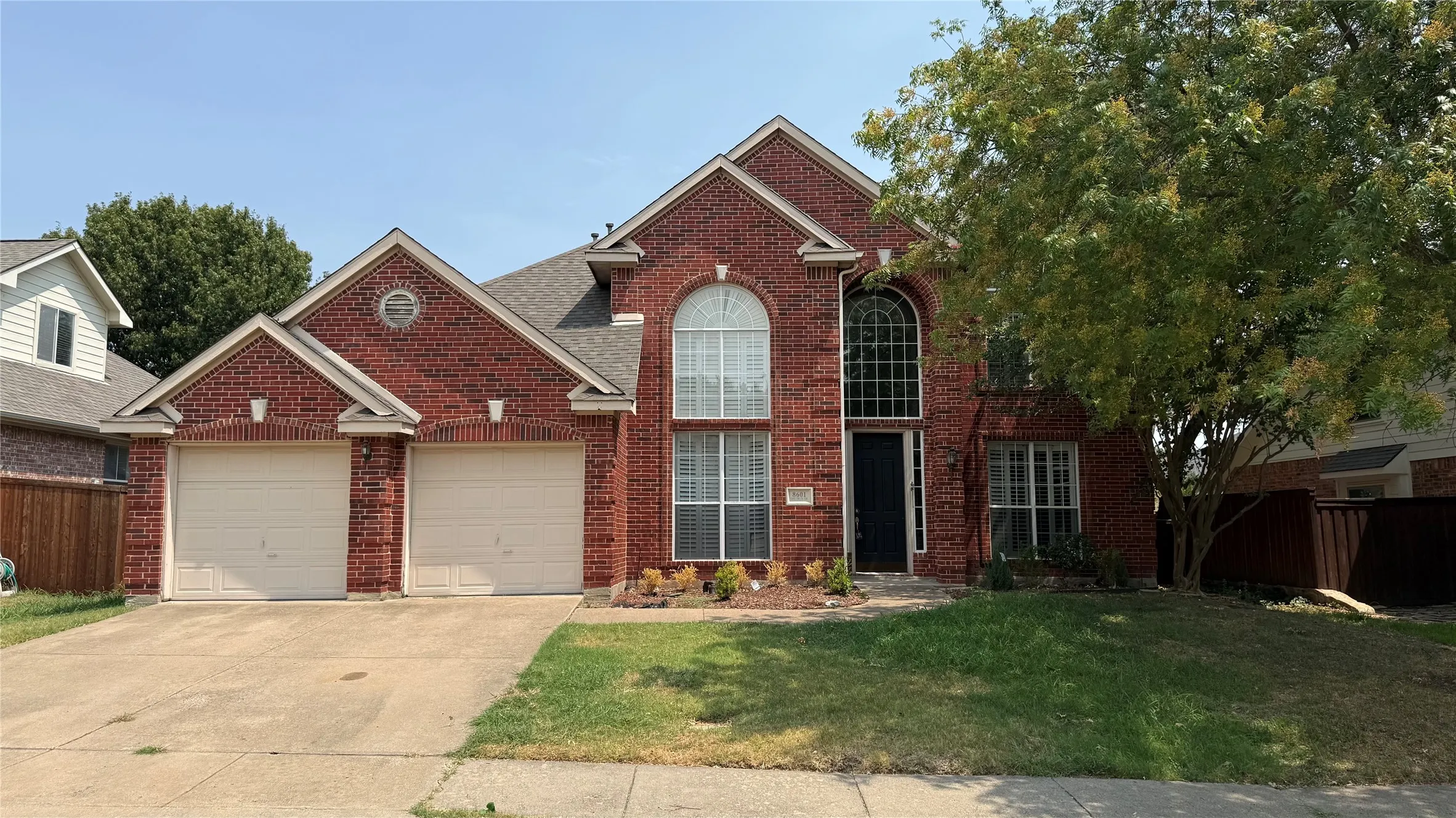 Brick exterior with an arched window above the entry, a two-car garage, and established landscaping