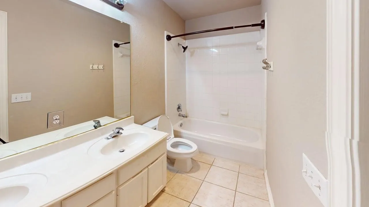 Dual vanity with integrated sinks, large wall-mounted mirror, ceramic tile flooring, and a bathtub with shower