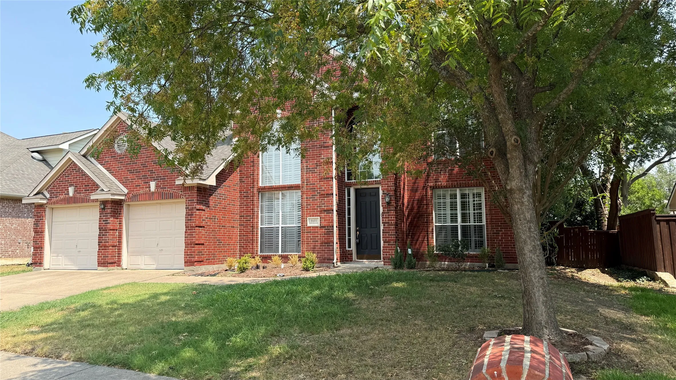 Traditional brick exterior with an attached two-car garage, prominent entry, and mature landscaping
