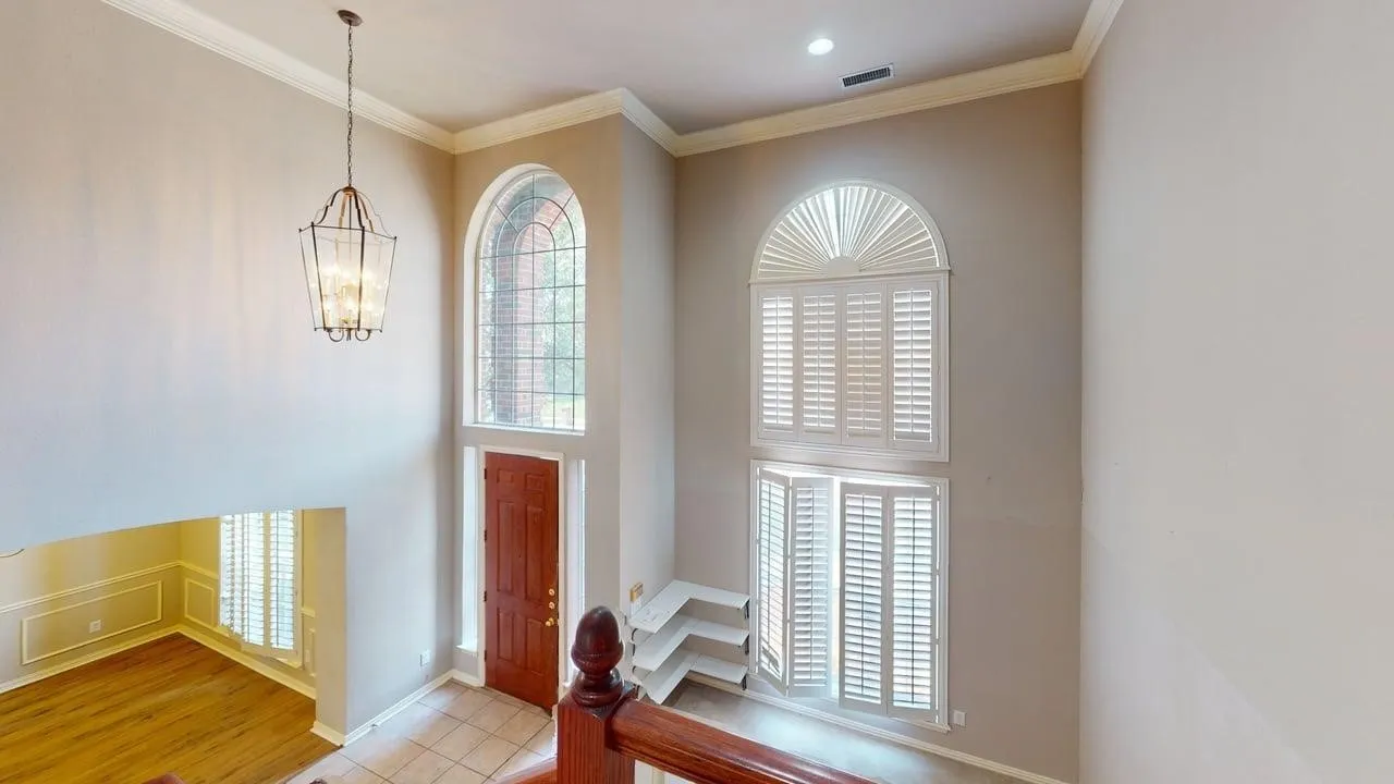 Two-story foyer with a tall arched window, white plantation shutters, and a chandelier light fixture