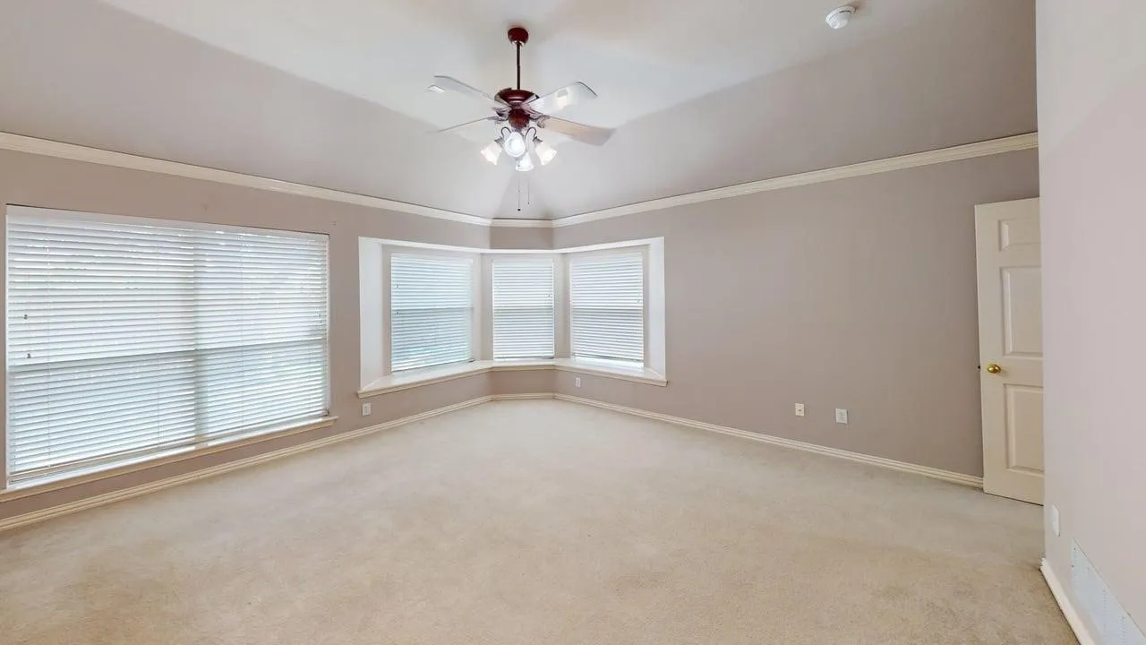 Vaulted ceiling with a ceiling fan, bay window, large window, and light-toned carpeting