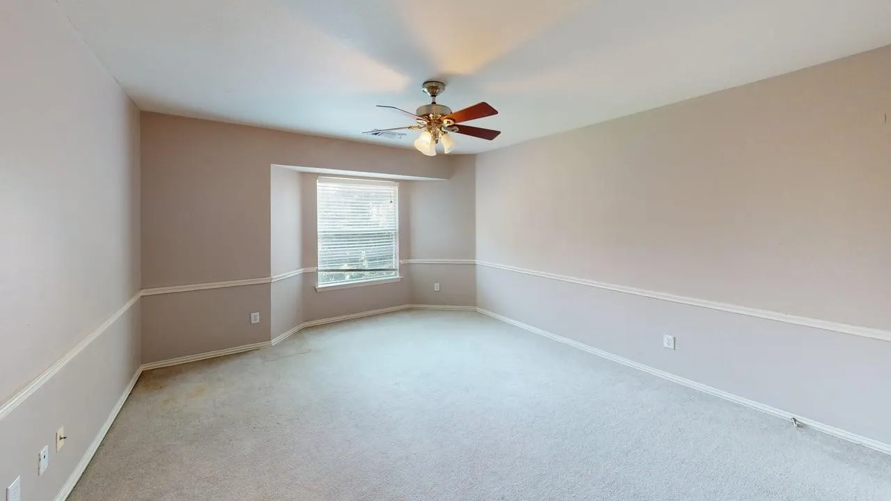 Spacious room featuring neutral carpeting, a bay window with blinds, and a ceiling fan with integrated lighting