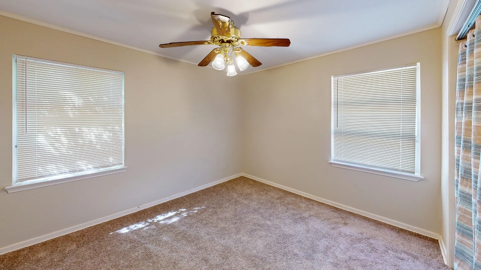 Neutral wall tones, carpet flooring, two windows with blinds, and a ceiling fan with integrated lighting
