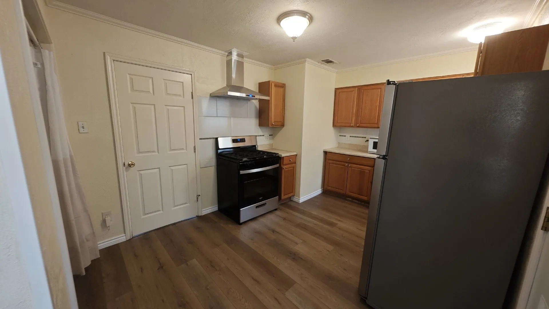 Kitchen featuring wood-finish flooring, wood cabinetry, a stainless steel range hood, and a built-in range