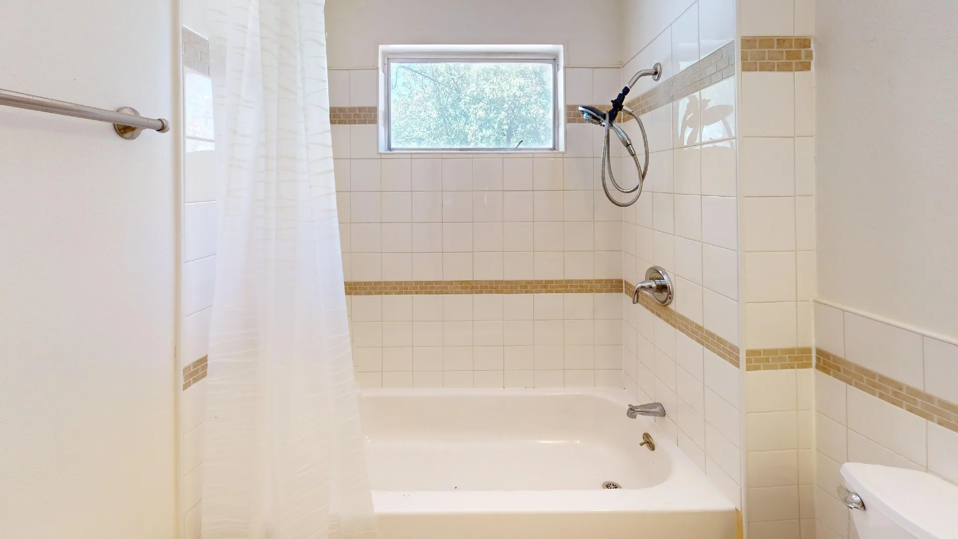 Bathtub with a shower/tub combination, white wall tiling, decorative accent tiling, and a window