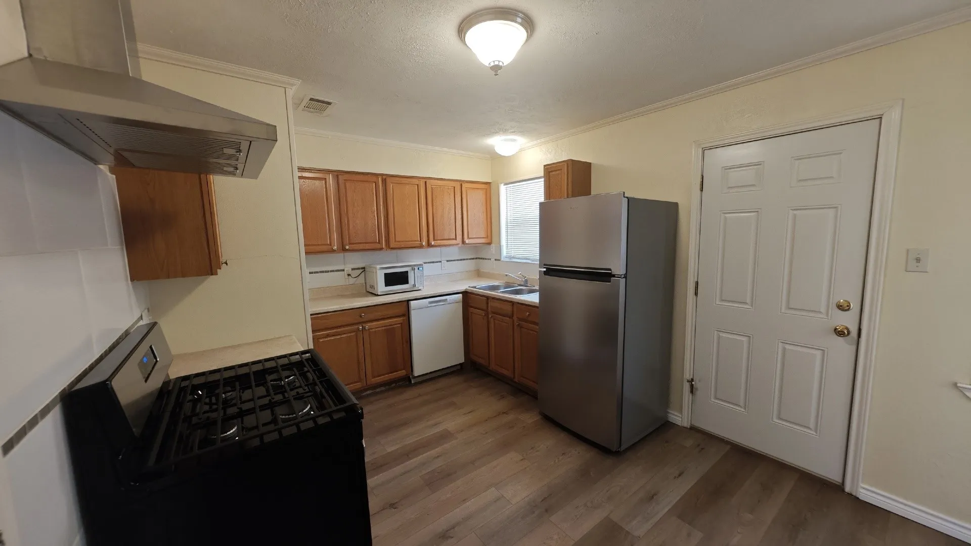 Kitchen featuring wood-finish flooring, wood cabinetry, stainless steel refrigerator, stainless steel range hood, and white tile backsplash