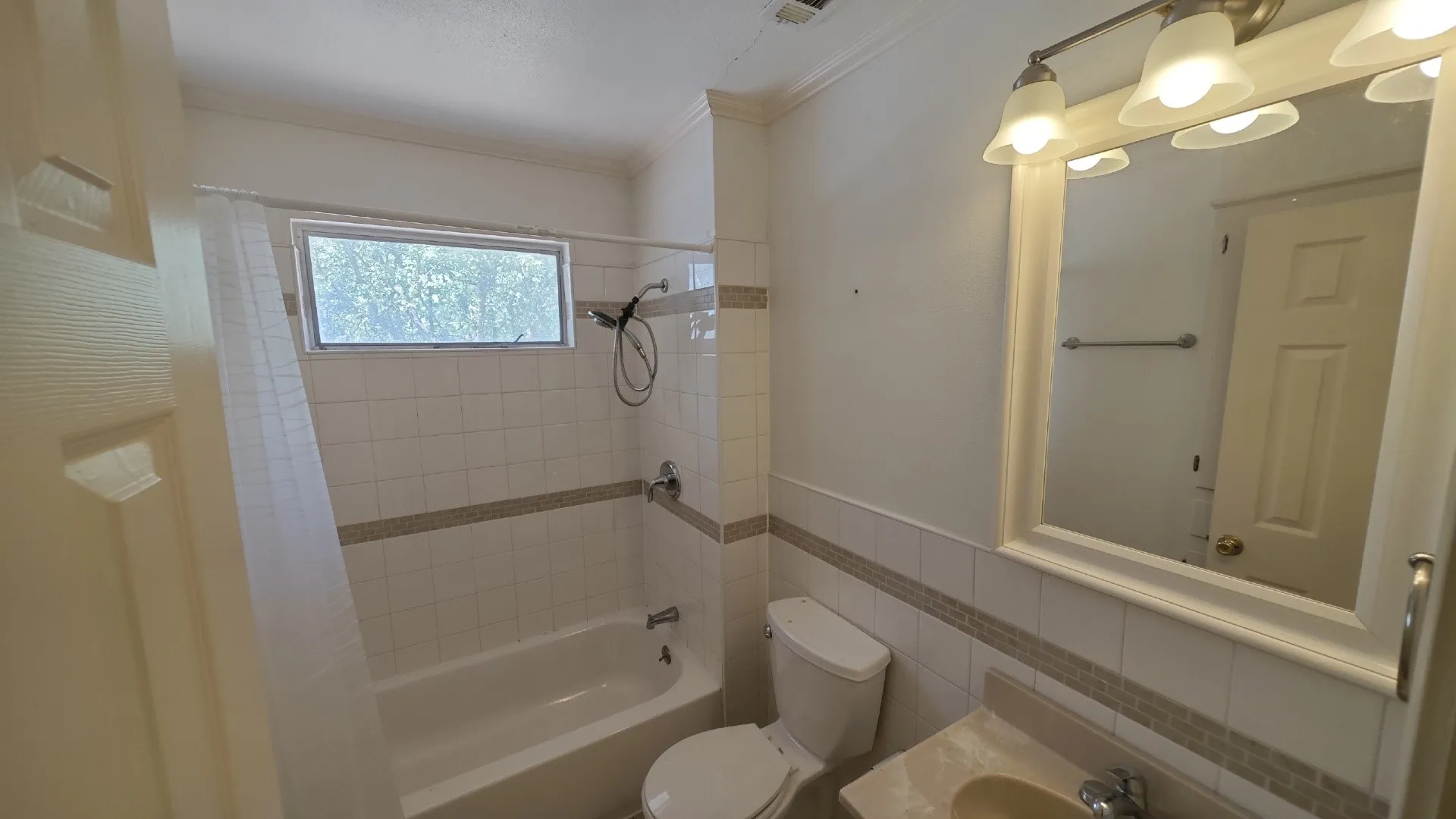 Bathroom featuring a tiled shower-tub combination with a window, a single vanity with a mounted mirror, and a three-light fixture