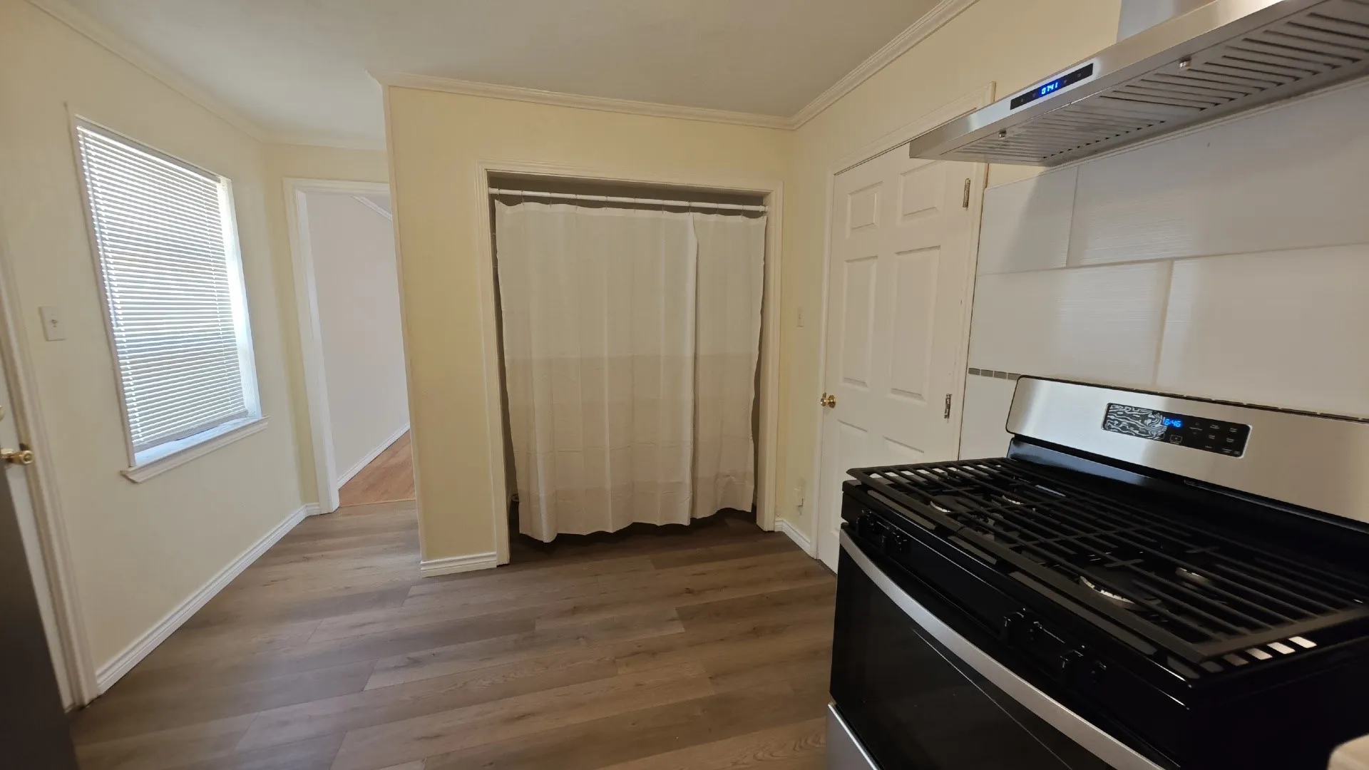Wood-finish flooring, white trim, stainless steel range hood, white subway tile backsplash, and a gas range
