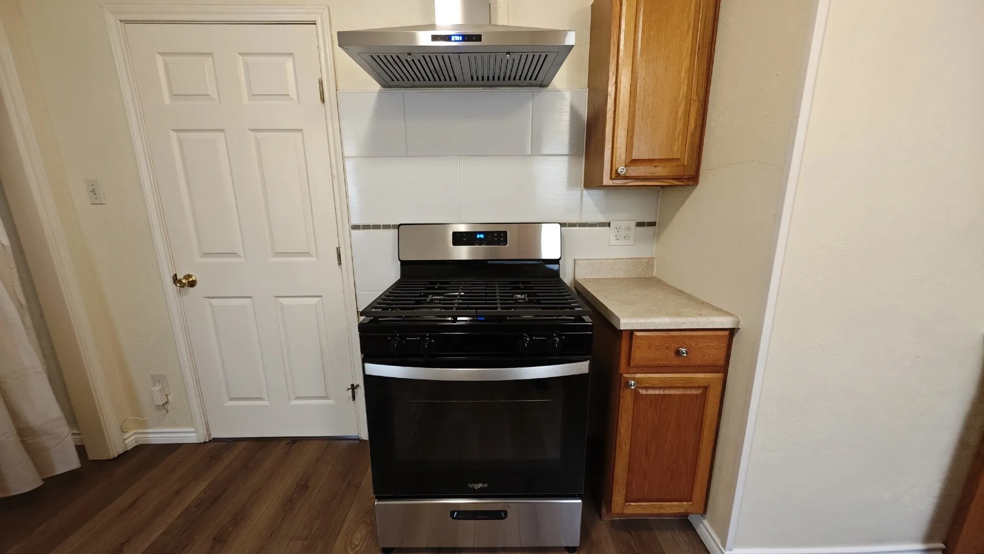 Stainless steel range with a coordinating hood, wood-finish flooring, and light-toned cabinetry