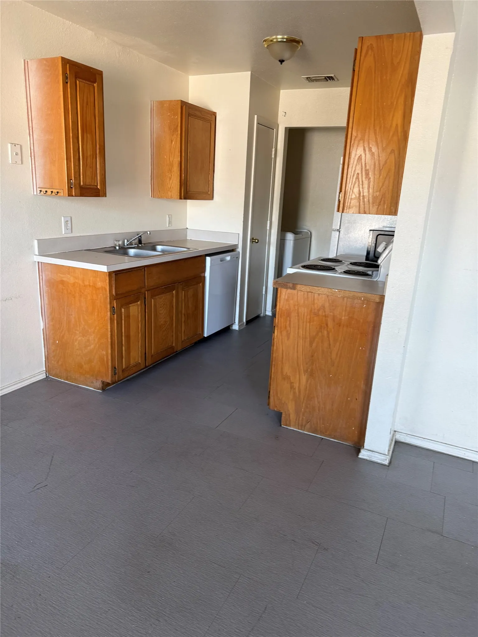 Unit B - Kitchen featuring wood-finish cabinetry, light-toned countertops, and a double basin sink. Laundry Room at the back.