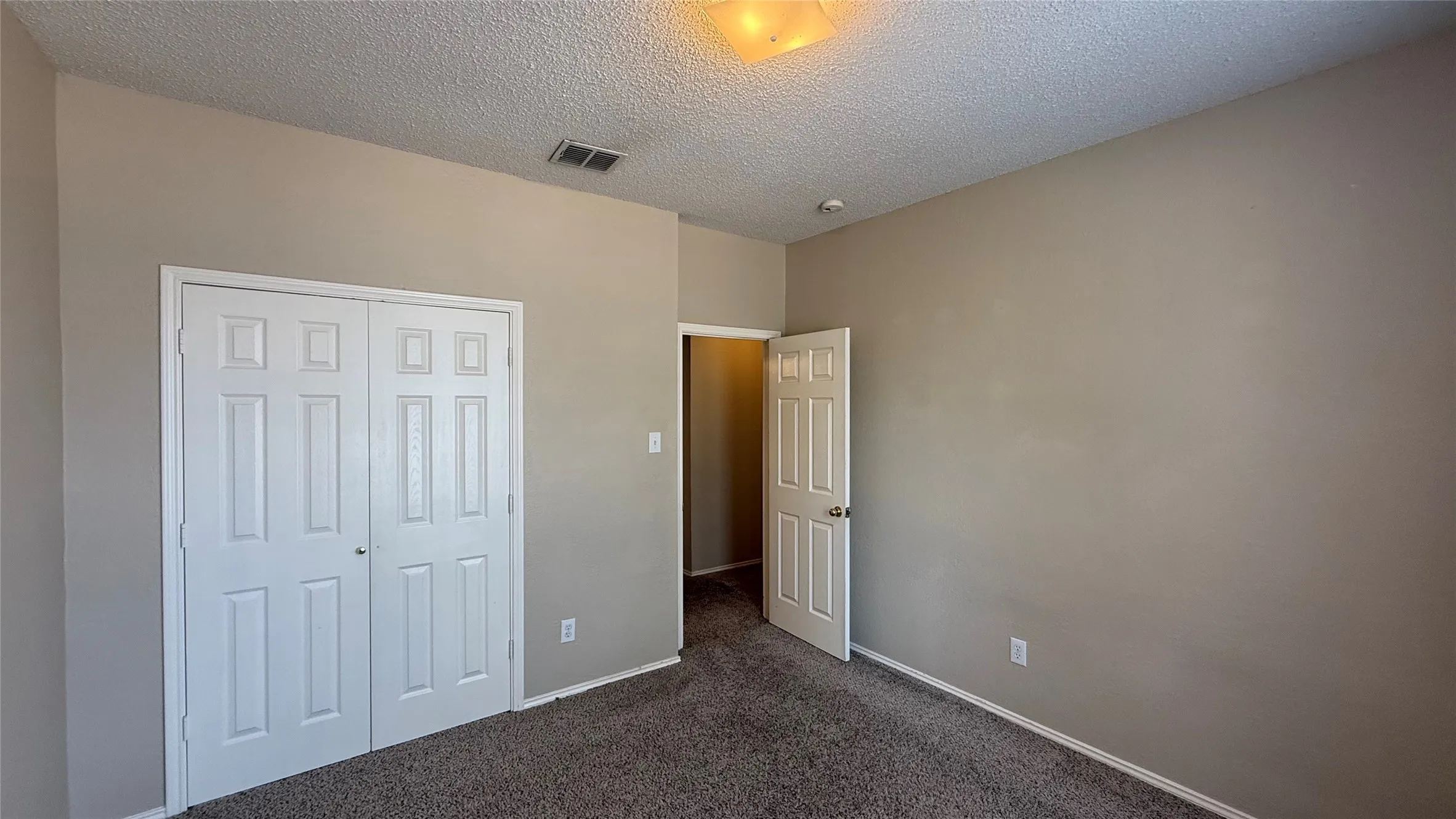 Neutral wall paint, textured ceiling, carpeted flooring, and a flush-mount light fixture