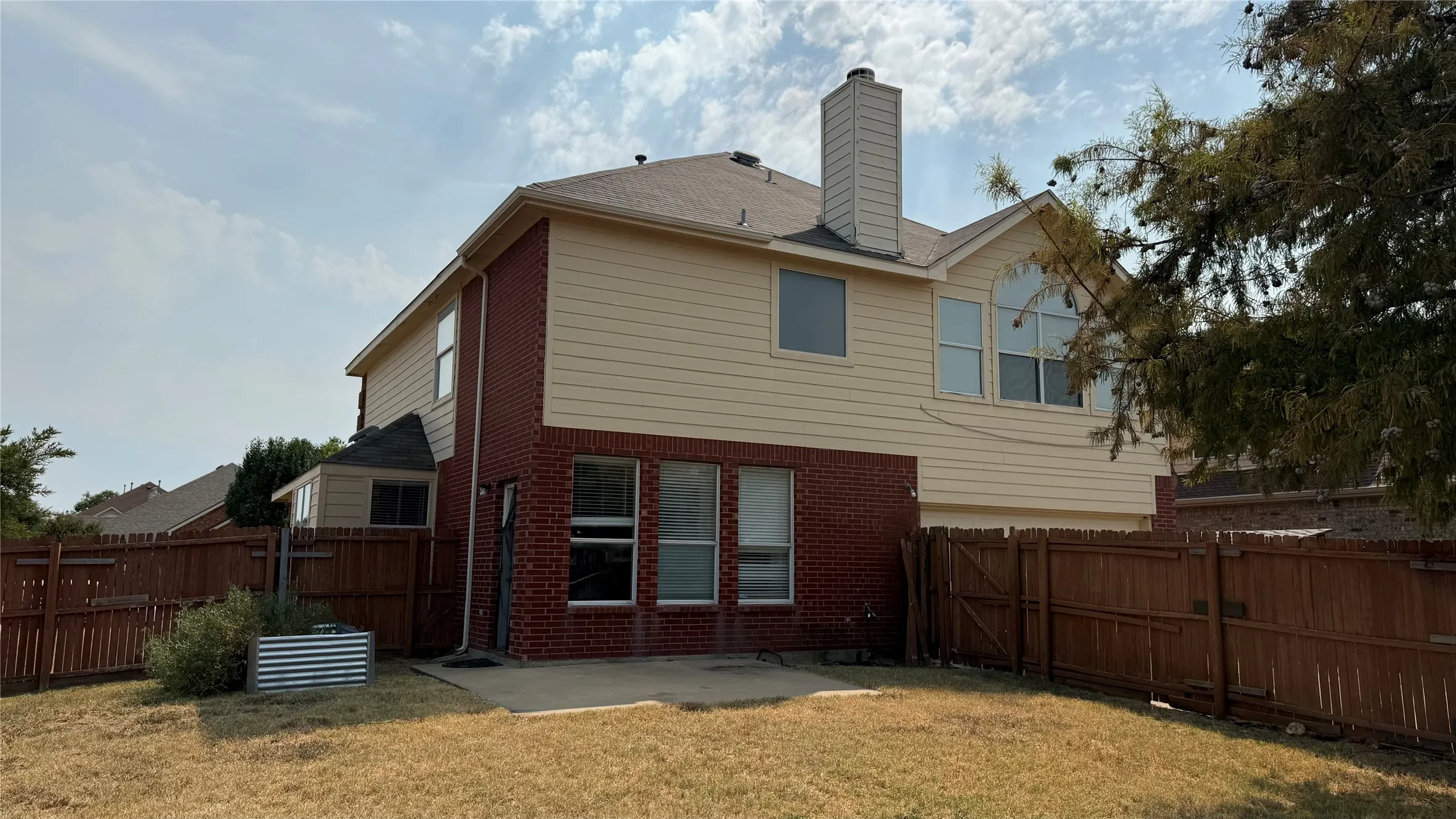 Two-story exterior with brick and siding facade, private wood fencing, ground-level patio, and chimney feature