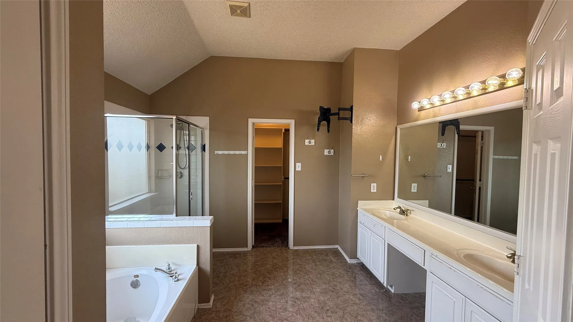 Dual vanity with integrated sinks, built-in soaking tub, glass-enclosed shower, vaulted ceiling, and built-in shelving