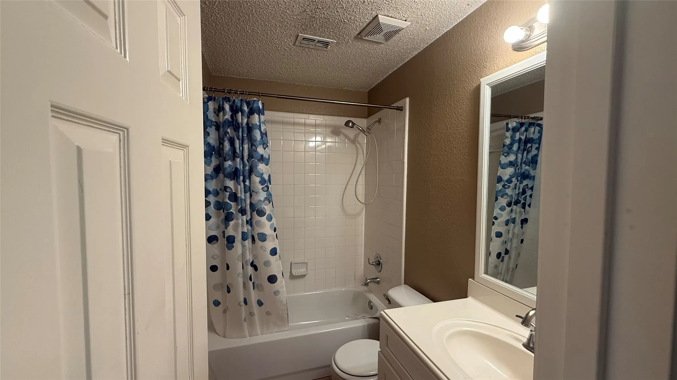Tub and shower combination with white subway tile surround, single vanity with integrated sink, and framed mirror