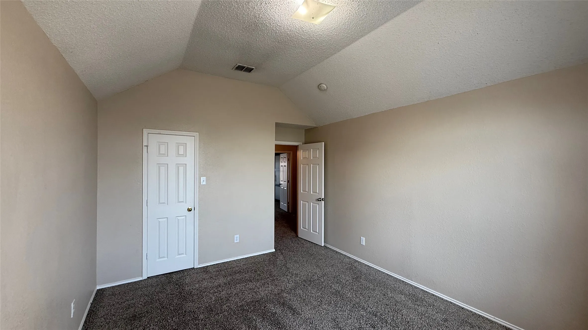 Vaulted ceiling, neutral tone walls, dark carpet flooring, white paneled doors, and a flush mount ceiling light fixture