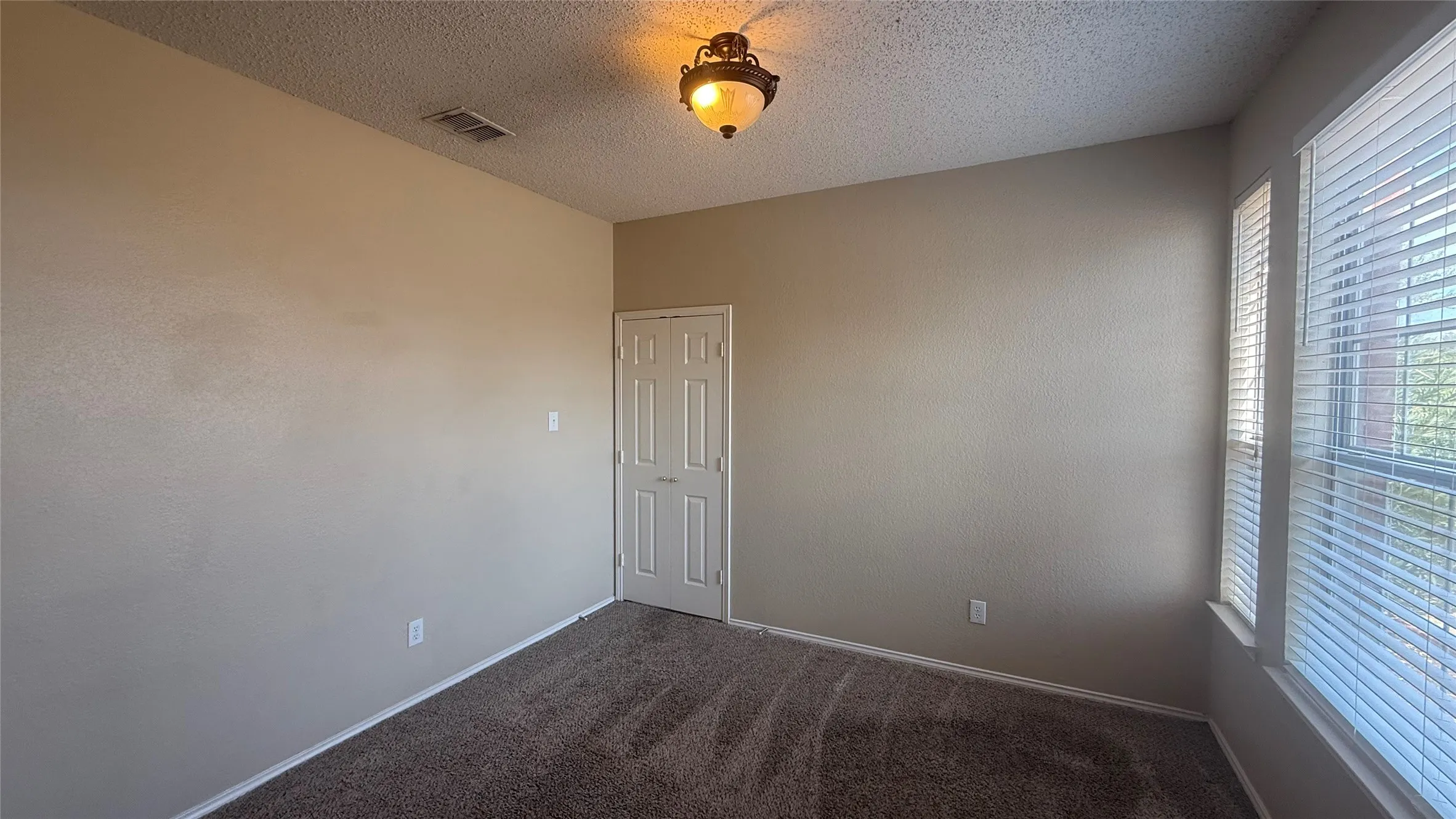 Textured walls, carpet flooring, a multi-pane window with blinds, and a built-in light fixture