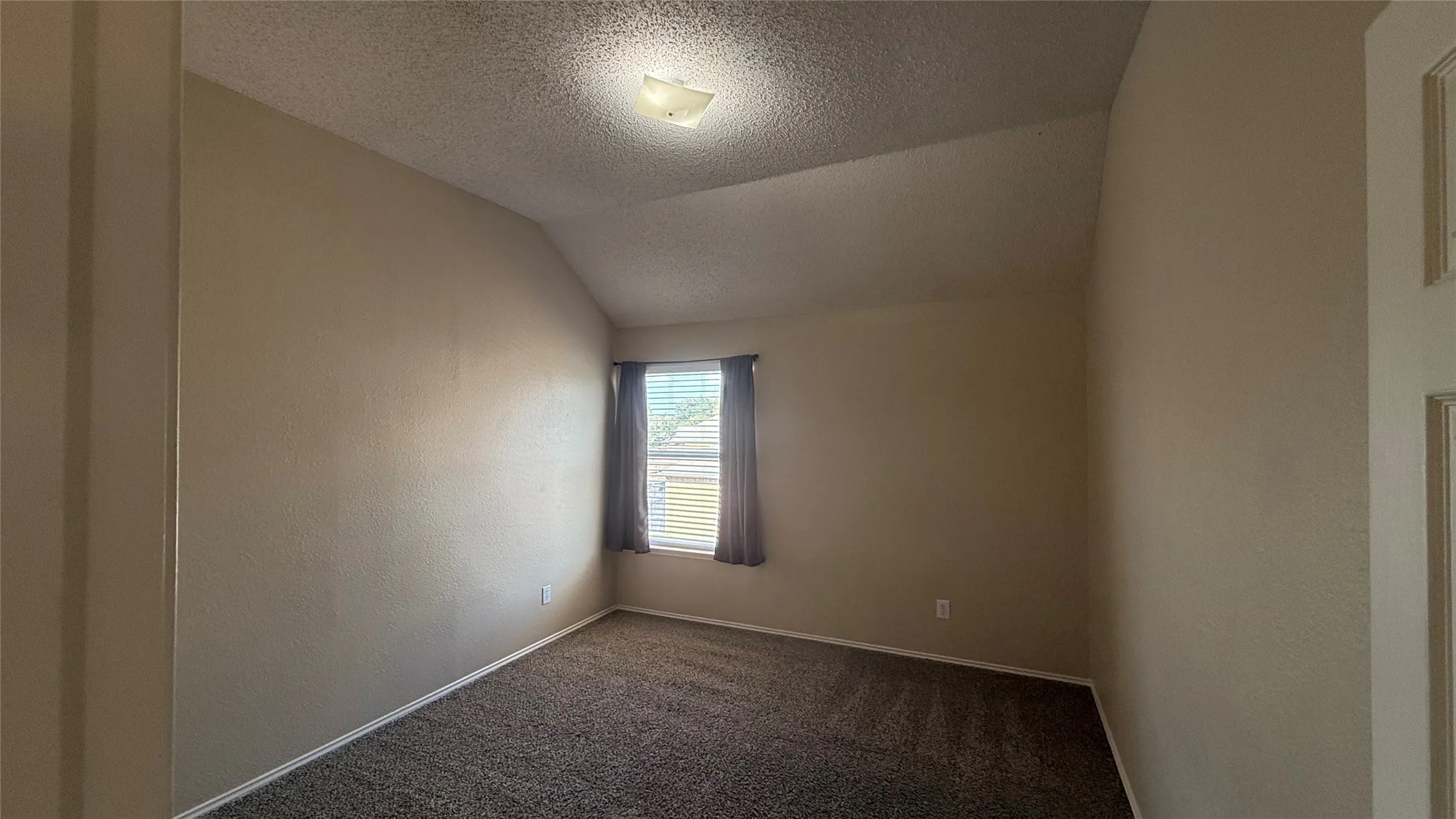 Vaulted ceiling with an attached light fixture, a window with blinds and curtains, and carpet flooring