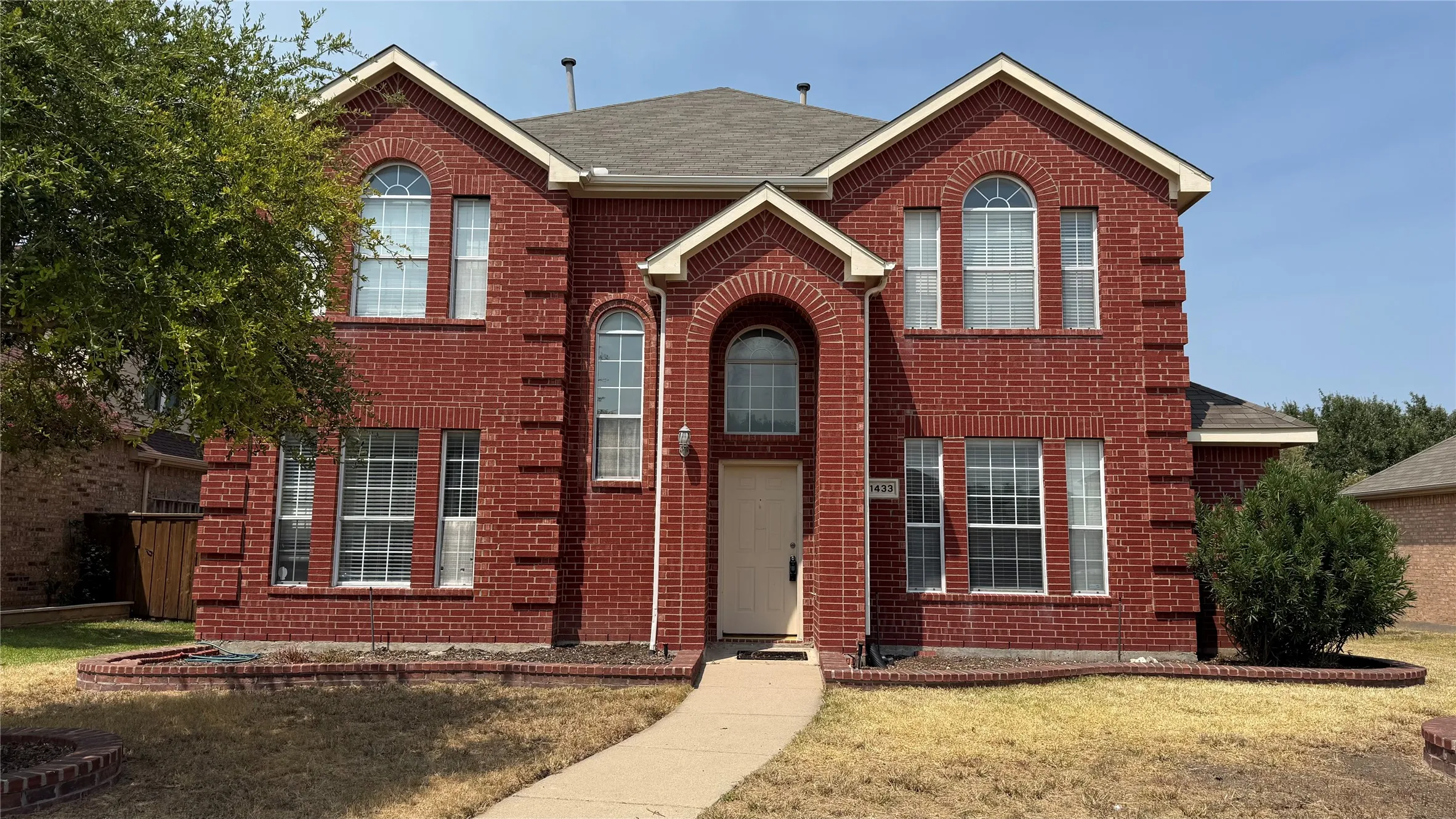 Red brick facade with arched windows, prominent entry archway, and a concrete pathway