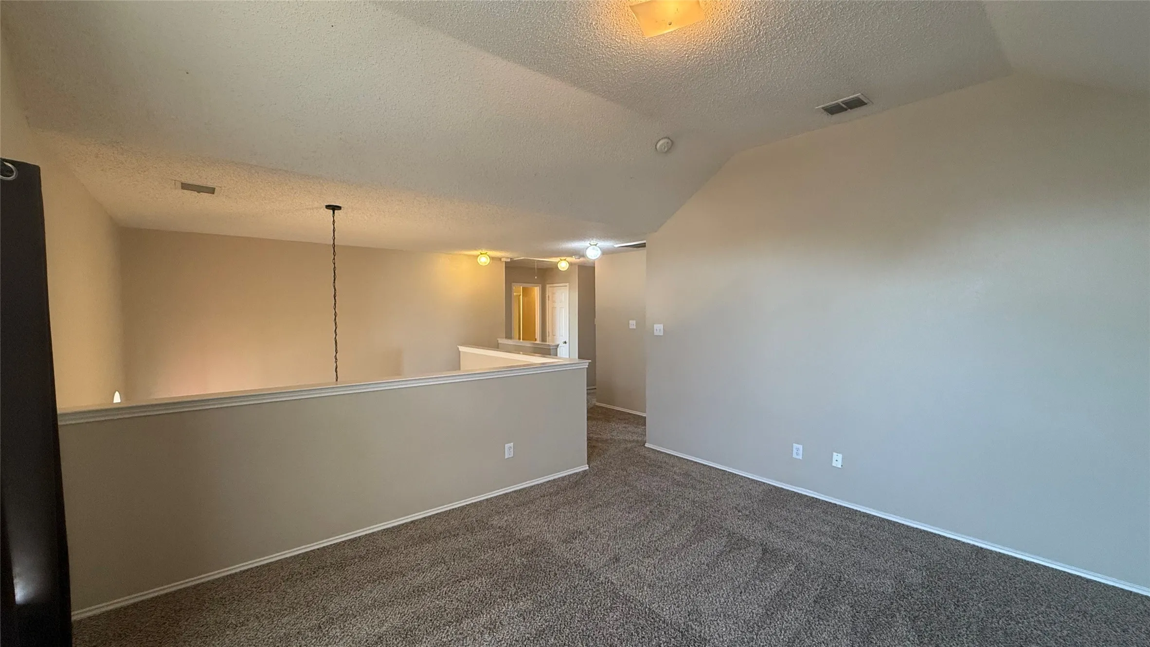 Carpeted flooring, vaulted ceiling, neutral wall tones, interior railing, and overhead lighting